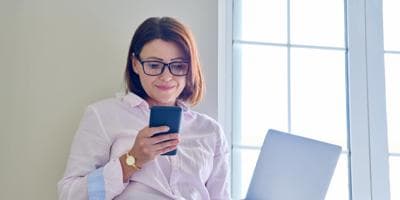 businesswoman leaning against wall looking at phone