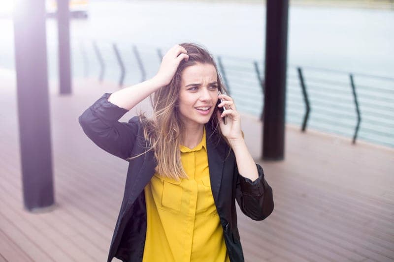 woman standing outside, listening to mobile phone, annoyed that it's a robocall